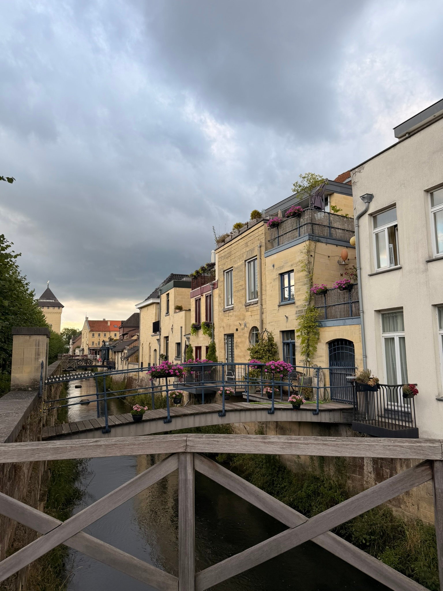 The Geul river running between marl-stone houses in Valkenburg with small private wooden bridges and the Berkelpoort tower in the distance