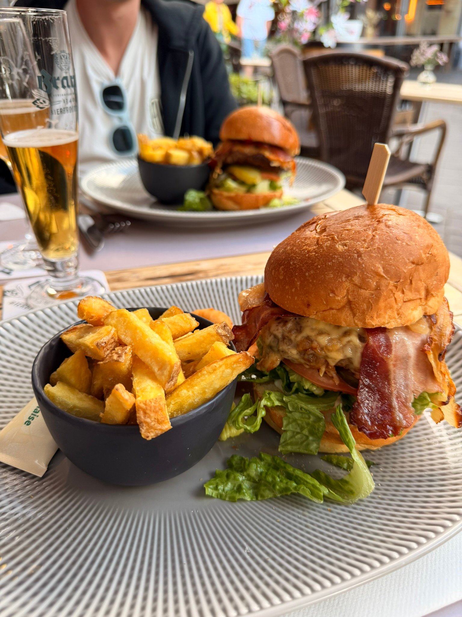A bacon cheeseburger with a bowl of thick-cut Dutch fries and a glass of beer on a Valkenburg terrace